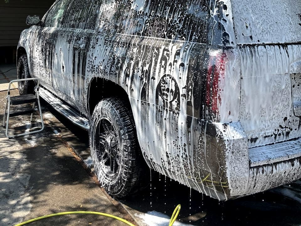 Detailer working spray product across a wet hood by hand