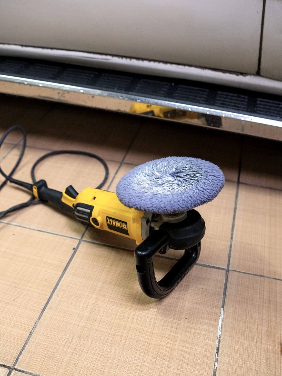 An electric polisher resting on the floor beside the vehicle it is working on