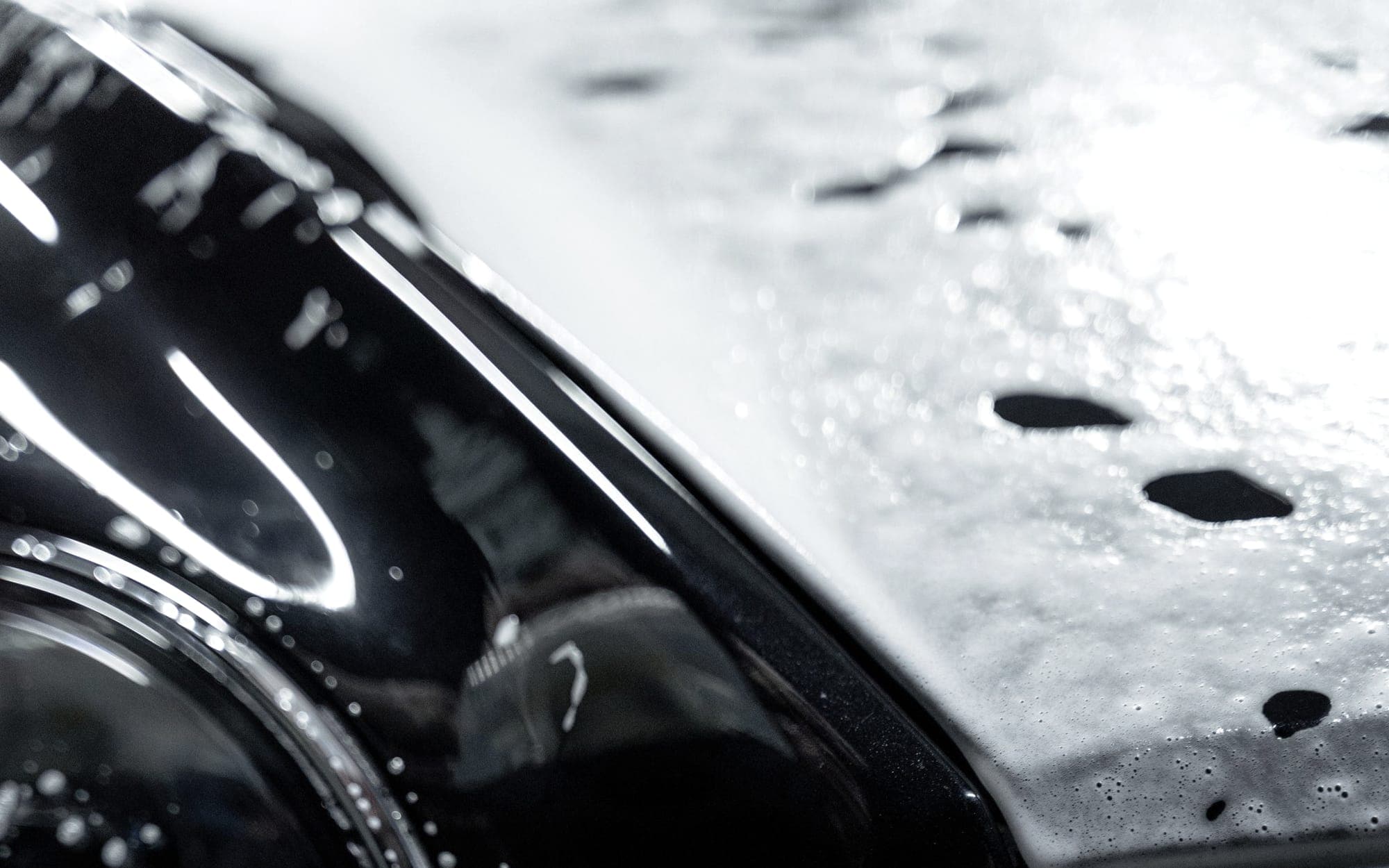 A dark car under snow foam, panels covered in suds